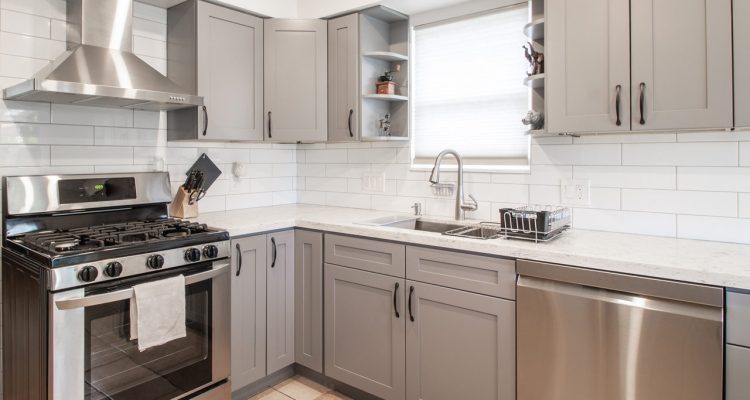 A compact modern kitchen featuring gray cabinetry, white subway tile backsplash, and stainless steel appliances, providing a functional and stylish cooking space.