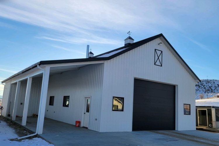 Custom white metal-frame shop building with large garage door and mountain backdrop by Jedd Shippy LLC